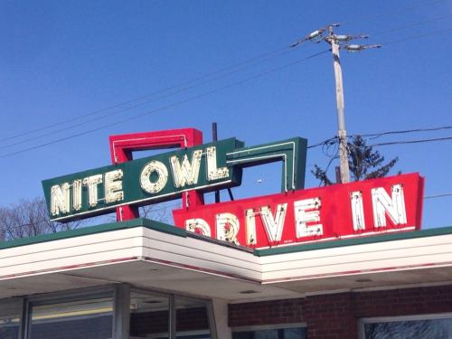 Vintage sign for "Nite Owl Drive In" with colorful letters against a clear blue sky.