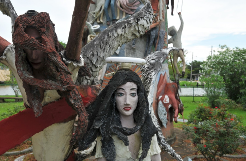 A surreal sculpture featuring figures with exaggerated features, set in a green outdoor space near water.