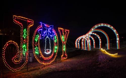 Colorful holiday lights spell "JOY" next to a glowing archway, set against a dark night sky.
