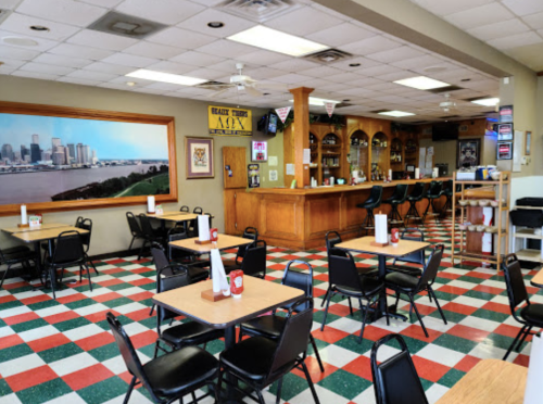 A cozy diner interior with checkered floors, empty tables, and a bar area featuring a cityscape mural.