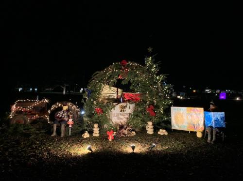 A festive display featuring a decorated wreath, lights, and holiday decorations in a dark outdoor setting.