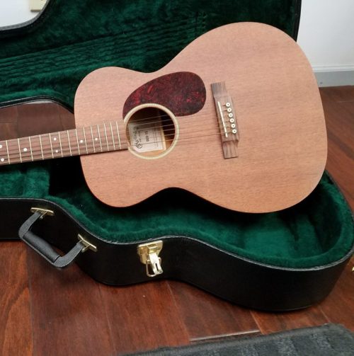 An acoustic guitar resting inside a green velvet-lined case, partially closed.