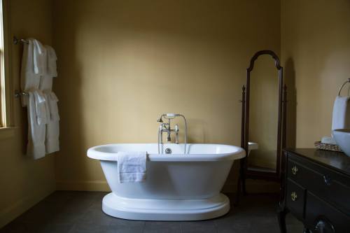 A modern bathroom featuring a freestanding white bathtub, towels on a rack, and a vintage mirror against a yellow wall.