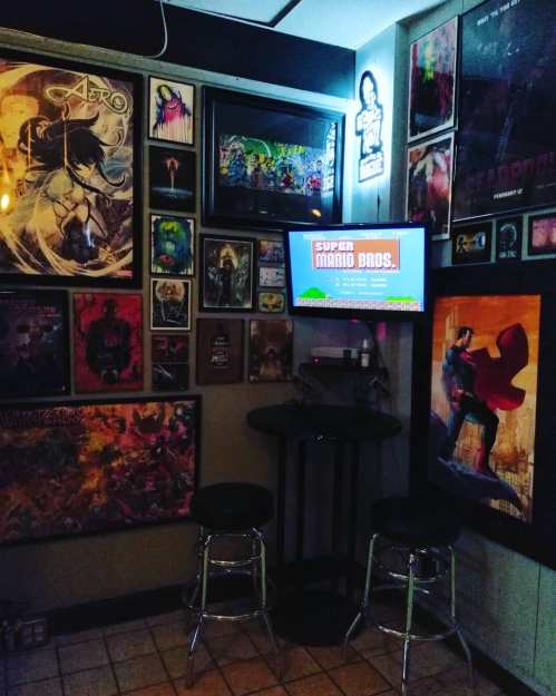 A cozy gaming corner with a TV displaying Super Mario Bros, surrounded by colorful posters and artwork on the walls.