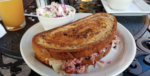 A toasted sandwich filled with meat, served with a side of coleslaw on a decorative table.
