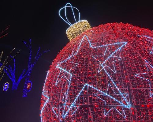 A large, illuminated Christmas ornament with red and blue lights, featuring a star design and a golden crown on top.