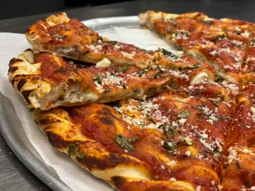 A close-up of a pizza with a crispy crust, topped with tomato sauce, herbs, and cheese, on a metal tray.