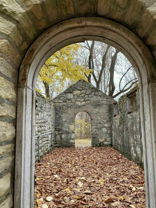 View through an arched doorway into stone ruins, surrounded by autumn leaves and trees with yellow foliage.