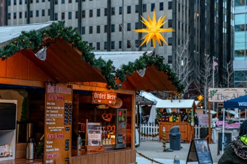 A festive market stall with a menu, decorated with garlands and a large star above, set in an urban environment.