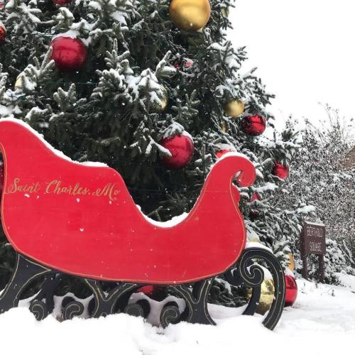 A red sleigh decorated with gold and red ornaments, surrounded by snow-covered trees in a winter setting.