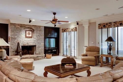 Cozy living room with a stone fireplace, comfortable seating, and large windows with blinds.