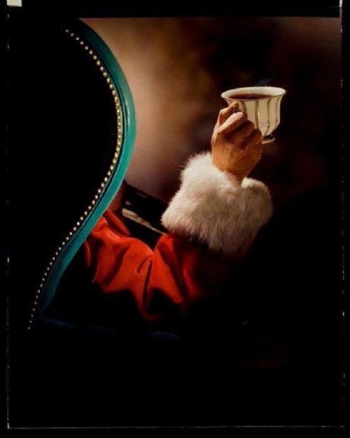 A hand in a fur-cuffed sleeve holds a steaming cup, partially obscured by a chair's backrest.