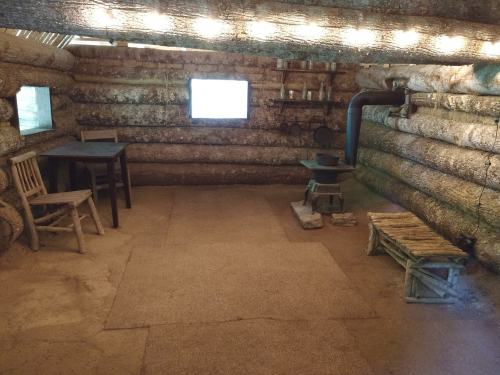 Interior of a rustic log cabin with a table, chairs, and a stove, illuminated by warm lights.