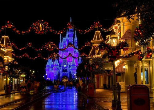 A festive scene of a lit-up castle at night, adorned with holiday decorations and glowing lights along a charming street.