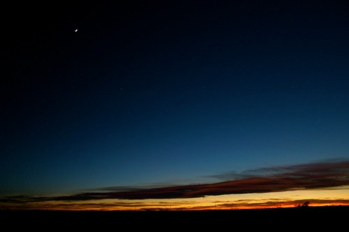 A serene twilight sky with a crescent moon and a bright star above a colorful horizon.