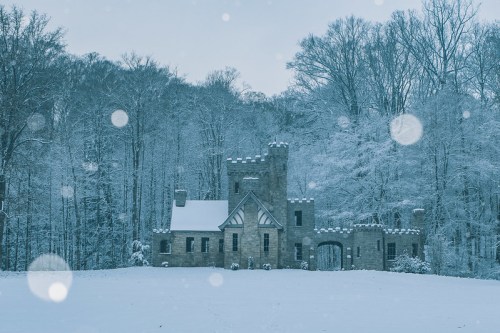 A snow-covered castle surrounded by trees, with soft snowflakes falling in a serene winter landscape.
