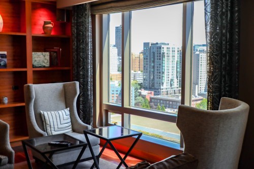 Cozy seating area with two armchairs and a glass table, overlooking a city skyline through large windows.