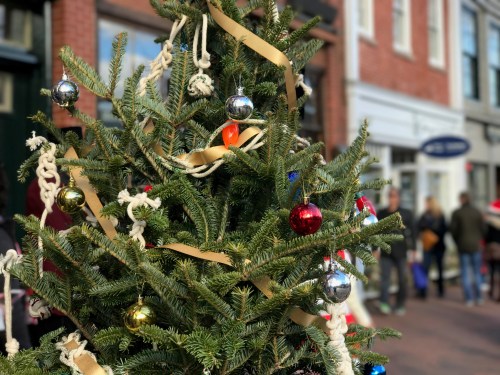 A decorated Christmas tree with colorful ornaments and ribbons, set against a festive street scene.