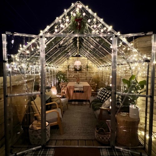 A cozy greenhouse at night, adorned with fairy lights, plants, and a table set for dining.