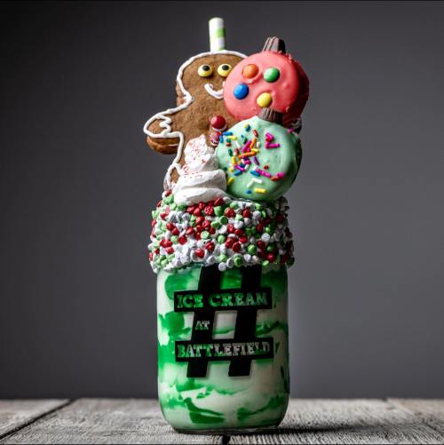 A festive milkshake topped with cookies, whipped cream, and colorful sprinkles in a jar with "Ice Cream at Battlefield" label.