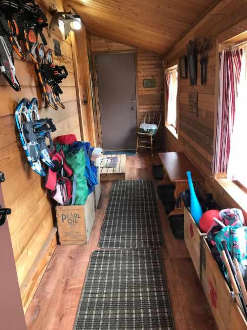 A cozy wooden hallway with snowshoes on the wall, storage boxes, and a small table near the door.
