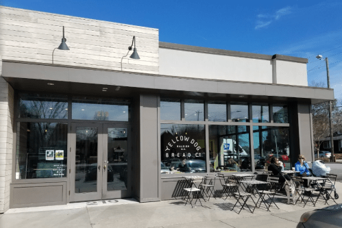 Exterior of Yellow Dog Bread Co. with large windows, outdoor seating, and a clear blue sky.