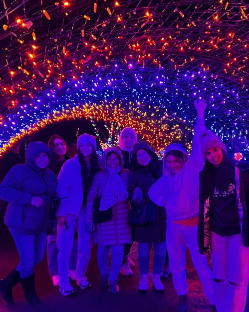 A group of people smiling and posing under a colorful, illuminated archway of lights.