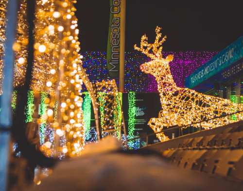A glowing reindeer made of lights surrounded by colorful holiday decorations.