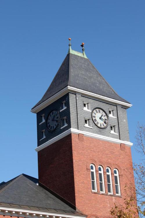 Clock tower with a peaked roof, featuring a large clock face, against a clear blue sky.