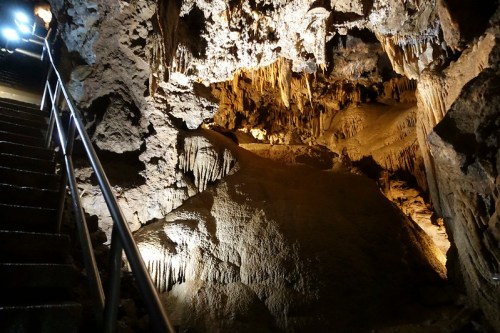 A dimly lit cave interior with stalactites and stalagmites, featuring a staircase on the left side.