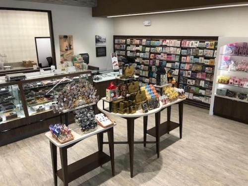 A cozy shop interior featuring display tables with various products and a wall of colorful cards in the background.
