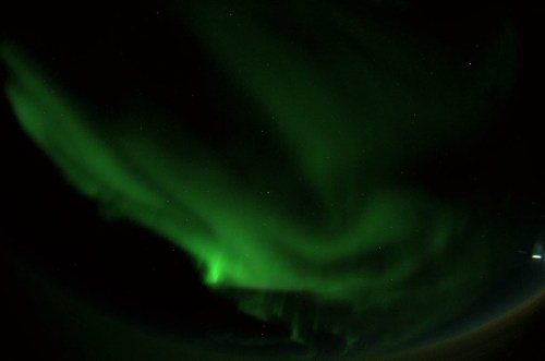 A vibrant green aurora borealis dances across a dark night sky, with scattered stars visible in the background.