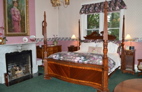 A cozy bedroom featuring a four-poster bed, floral decor, a fireplace, and elegant furnishings.