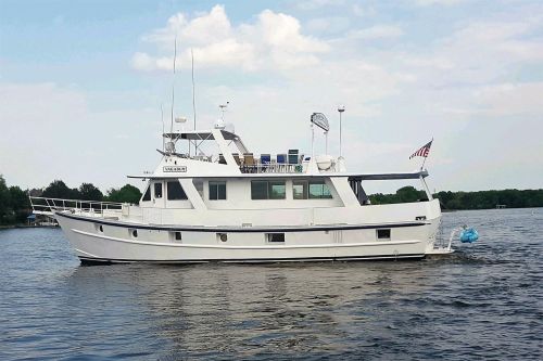A large white motor yacht cruising on calm water under a partly cloudy sky.