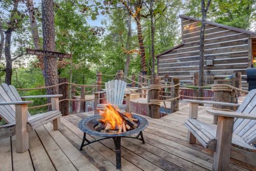 A cozy outdoor deck with wooden chairs and a fire pit, surrounded by trees and a rustic cabin in the background.