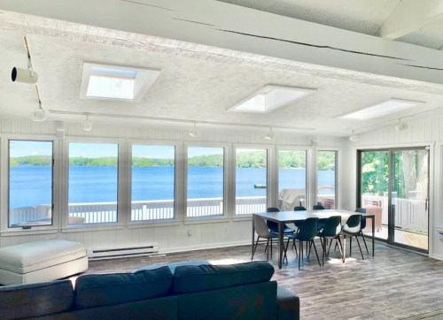 Bright, modern interior with large windows overlooking a serene lake, featuring a dining area and comfortable seating.