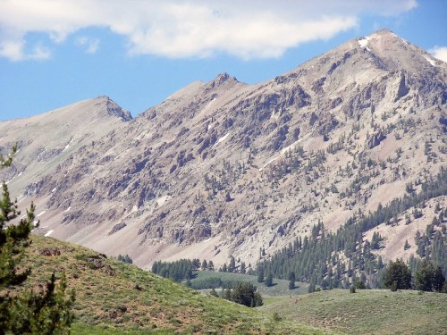 A scenic view of rugged mountains with rocky peaks and green hills in the foreground under a blue sky.