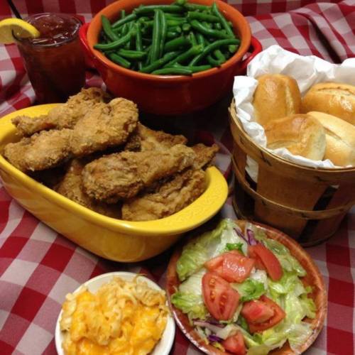 A hearty meal featuring fried chicken, green beans, rolls, macaroni and cheese, and a fresh salad on a checkered tablecloth.