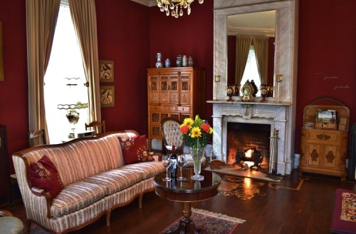 Cozy living room with red walls, vintage furniture, a fireplace, and a vase of flowers on a round table.
