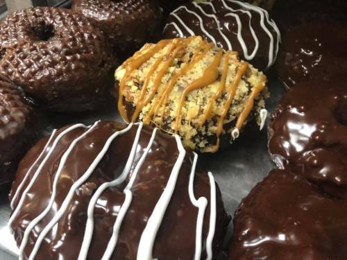 A variety of chocolate-covered donuts, including one topped with caramel and crumbled cookie.