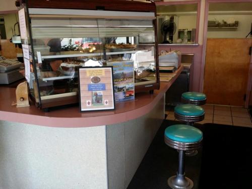 A diner counter with a glass display case, menu sign, and teal bar stools in a cozy, retro setting.