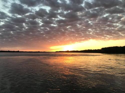 A serene sunset over a calm river, with vibrant colors reflecting on the water and a dramatic cloud-filled sky.
