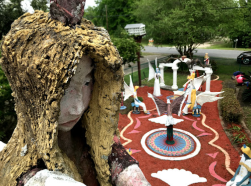 A colorful outdoor garden featuring whimsical sculptures and a circular design, surrounded by greenery and pathways.