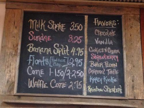 Chalkboard menu listing ice cream flavors and prices for milkshakes, sundaes, banana splits, and more.