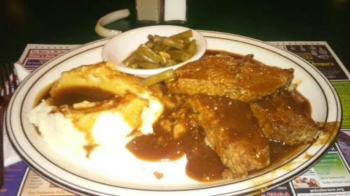 A plate of meatloaf with gravy, mashed potatoes, and green beans served in a diner setting.