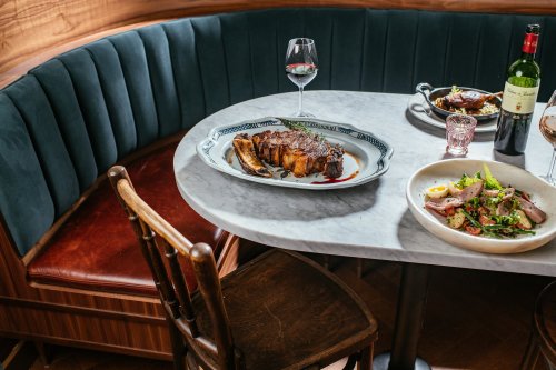 A beautifully set table featuring a roast, salad, and wine, with a cozy booth in the background.