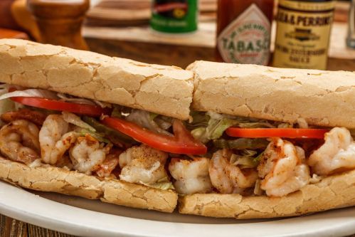 A close-up of a shrimp sandwich with lettuce, tomato, and spices, served on a toasted hoagie roll.