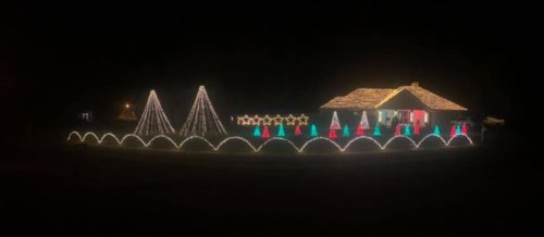 A house decorated with colorful Christmas lights, featuring trees, stars, and festive shapes against a dark night sky.