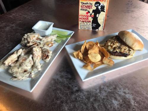 A plate of chicken wings with dipping sauce and celery, alongside a burger topped with cheese and potato chips.