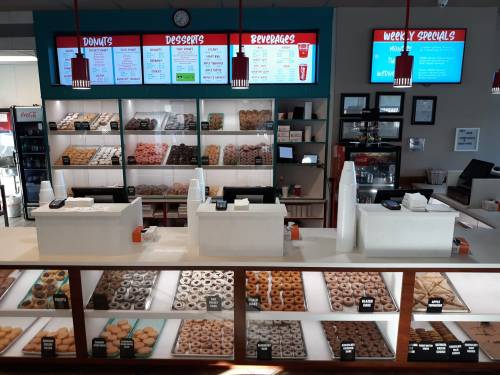 A bright donut shop display with various donuts, a menu board, and a counter for ordering beverages and desserts.
